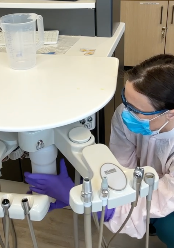 Dental assistant placing a Sterisil Straw into a water bottle system with gloves, demonstrating routine waterline maintenance.